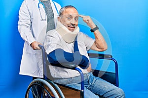 Handsome senior man with beard sitting on wheelchair with neck collar smiling pointing to head with one finger, great idea or