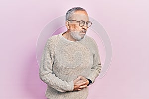 Handsome senior man with beard wearing casual sweater and glasses with hand on stomach because indigestion, painful illness