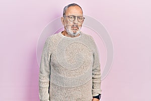 Handsome senior man with beard wearing casual sweater and glasses relaxed with serious expression on face