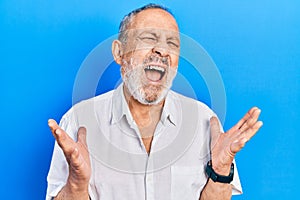 Handsome senior man with beard wearing casual white shirt crazy and mad shouting and yelling with aggressive expression and arms