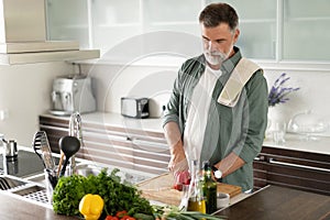 Handsome senior man cooking at home preparing salad in kitchen