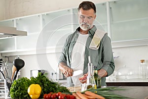 Handsome senior man cooking at home preparing salad in kitchen