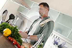 Handsome senior man cooking at home preparing salad in kitchen