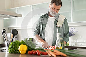 Handsome senior man cooking at home preparing salad in kitchen