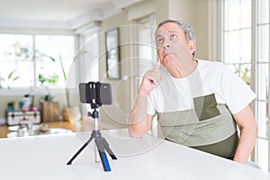 Handsome senior man doing video conference talking to the smartphone camera with hand on chin thinking about question, pensive