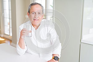 Handsome senior man drinking a fresh glass of water at home with a confident expression on smart face thinking serious