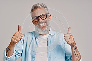 Handsome senior man in eyeglasses keeping thumbs up and smiling