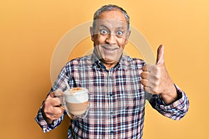 Handsome senior man with grey hair drinking a cup coffee approving doing positive gesture with hand, thumbs up smiling and happy