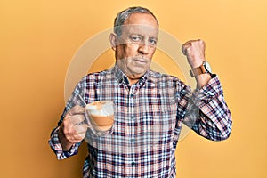 Handsome senior man with grey hair drinking a cup coffee strong person showing arm muscle, confident and proud of power