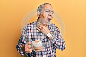 Handsome senior man with grey hair drinking a cup coffee touching painful neck, sore throat for flu, clod and infection