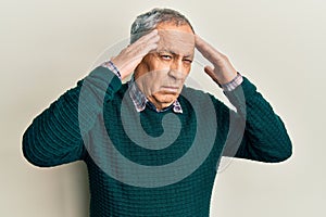 Handsome senior man with grey hair wearing casual sweater with hand on head, headache because stress