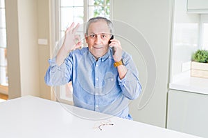 Handsome senior man having a conversation speaking on smartphone doing ok sign with fingers, excellent symbol