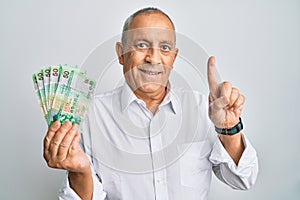 Handsome senior man holding 50 hong kong dollars banknotes smiling with an idea or question pointing finger with happy face,