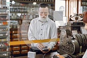 Handsome senior man holding cashless payment terminal in hands and paying for medicines, standing in beautiful ancient