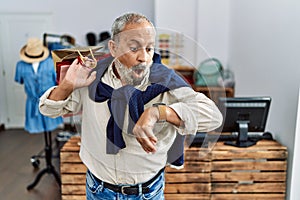 Handsome senior man holding shopping bags at boutique shop looking at the watch time worried, afraid of getting late