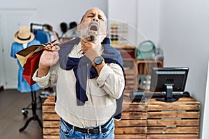 Handsome senior man holding shopping bags at boutique shop touching painful neck, sore throat for flu, clod and infection