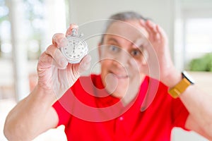 Handsome senior man holding stopwach showing countdown with happy face smiling doing ok sign with hand on eye looking through