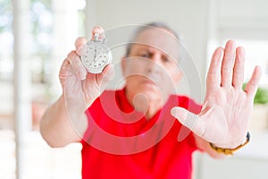 Handsome senior man holding stopwach showing countdown with open hand doing stop sign with serious and confident expression,