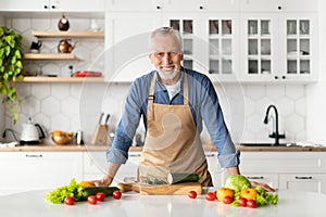 Handsome senior man posing at kitchen interior while cooking healthy food