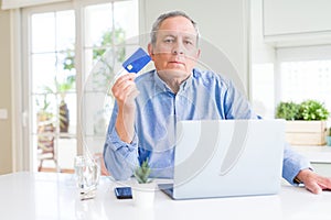 Handsome senior man shopping online using credit card and laptop at home with a confident expression on smart face thinking