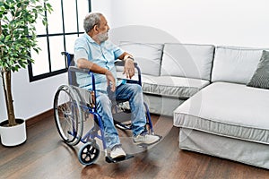 Handsome senior man sitting on wheelchair at the living room looking to side, relax profile pose with natural face with confident