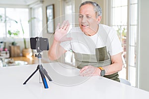 Handsome senior man waving hello to the smartphone camera doing video smiling very happy