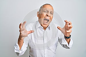 Handsome senior man wearing casual white shirt shouting frustrated with rage, hands trying to strangle, yelling mad
