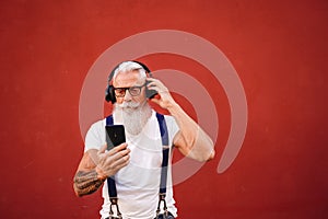 Handsome senior man with white beard, mustache and tattoos listening to music with headphones and mobile phone. Concept of elderly