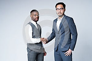 Handsome serious african american and asian businessmen agree to a contract shaking hands and looking at the camera