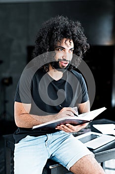 Handsome serious african american man with afro hairstyle holding a notebook in his hands and writes in it