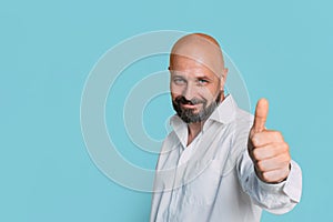 Handsome serious middle-aged man in a white shirt shows a thumb up to the camera on a blue background with copy space