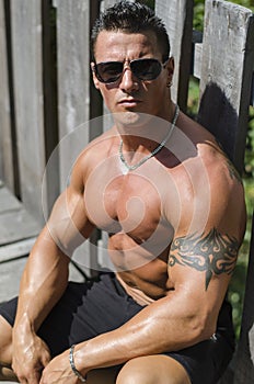 Handsome, serious muscleman sitting against wood