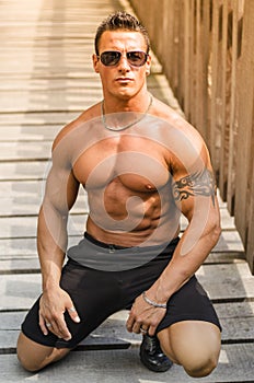 Handsome, serious muscleman sitting against wood