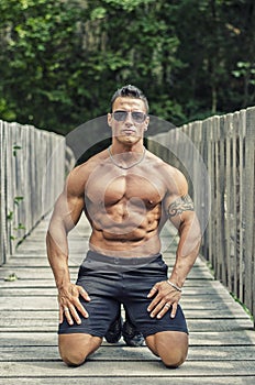 Handsome, serious muscleman sitting against wood