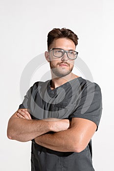 Handsome serious professional young male with arms crossed, physician practitioner in glasses on white studio background