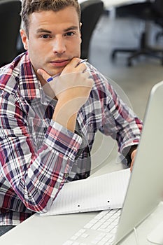 Handsome serious student using computer taking notes