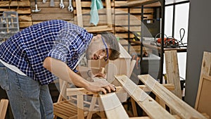 Handsome, serious, young arab man working diligently, sanding wood plank at the heart of his busy, indoor carpentry workshop