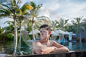 Handsome serious young man in the swimming pool at tropical island luxury resort