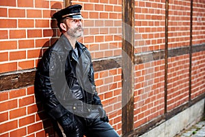 Handsome sexy bearded man dressed in black leather leaning against brick wall