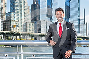 A handsome, sexy, middle age businessman with mustache and beard is standing in the front of a business district, smilingly photo