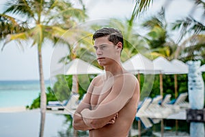 Handsome sexy young man standing near swimming pool at the tropical island