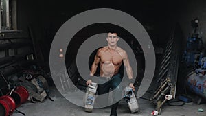 A handsome shirtless firefighter doing lunges holding a firehose in each hand. Fire-fighting equipment on the background