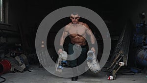 A handsome shirtless firefighter doing lunges holding a firehose in each hand. Fire-fighting equipment on the background