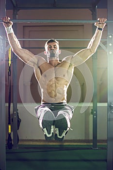 Handsome shirtless man doing pull ups in the L-sit position on horizontal bar outdoors at night. Calisthenics training