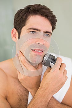 Handsome shirtless man shaving with electric razor