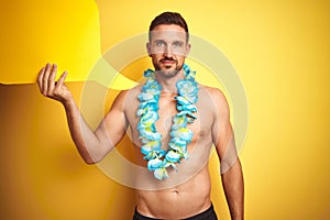 Handsome shirtless man wearing hawaiian lei holding speech bubble over yellow background with a confident expression on smart face