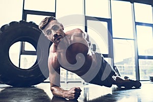 handsome shirtless sportsman doing plank on one hand photo