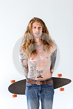 handsome shirtless tattooed sportsman with ginger hair standing with longboard