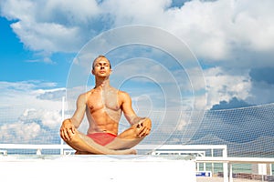 Handsome Shirtless Young Man During Meditation or Doing an Outdoor Yoga Exercise Sitting against the blue sky.