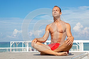 Handsome Shirtless Young Man During Meditation or Doing an Outdoor Yoga Exercise Sitting against the blue sky.